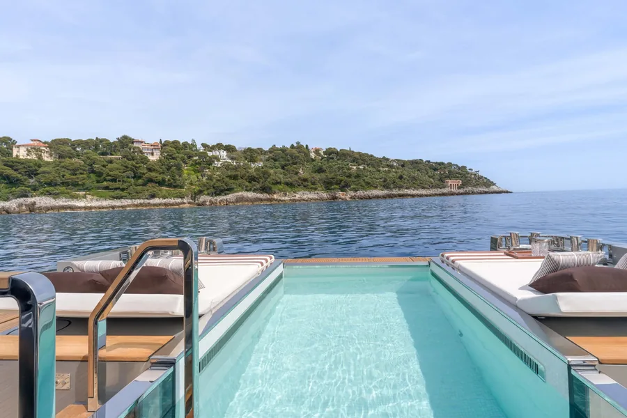 Pool on deck of the Riva 54Metri with sun loungers and a view of a wooded coast