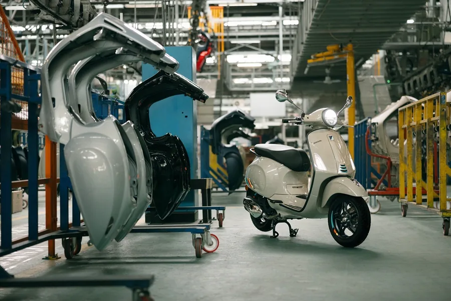 Детали кузова Vespa Primavera на стойке рядом с готовым скутером в цехе